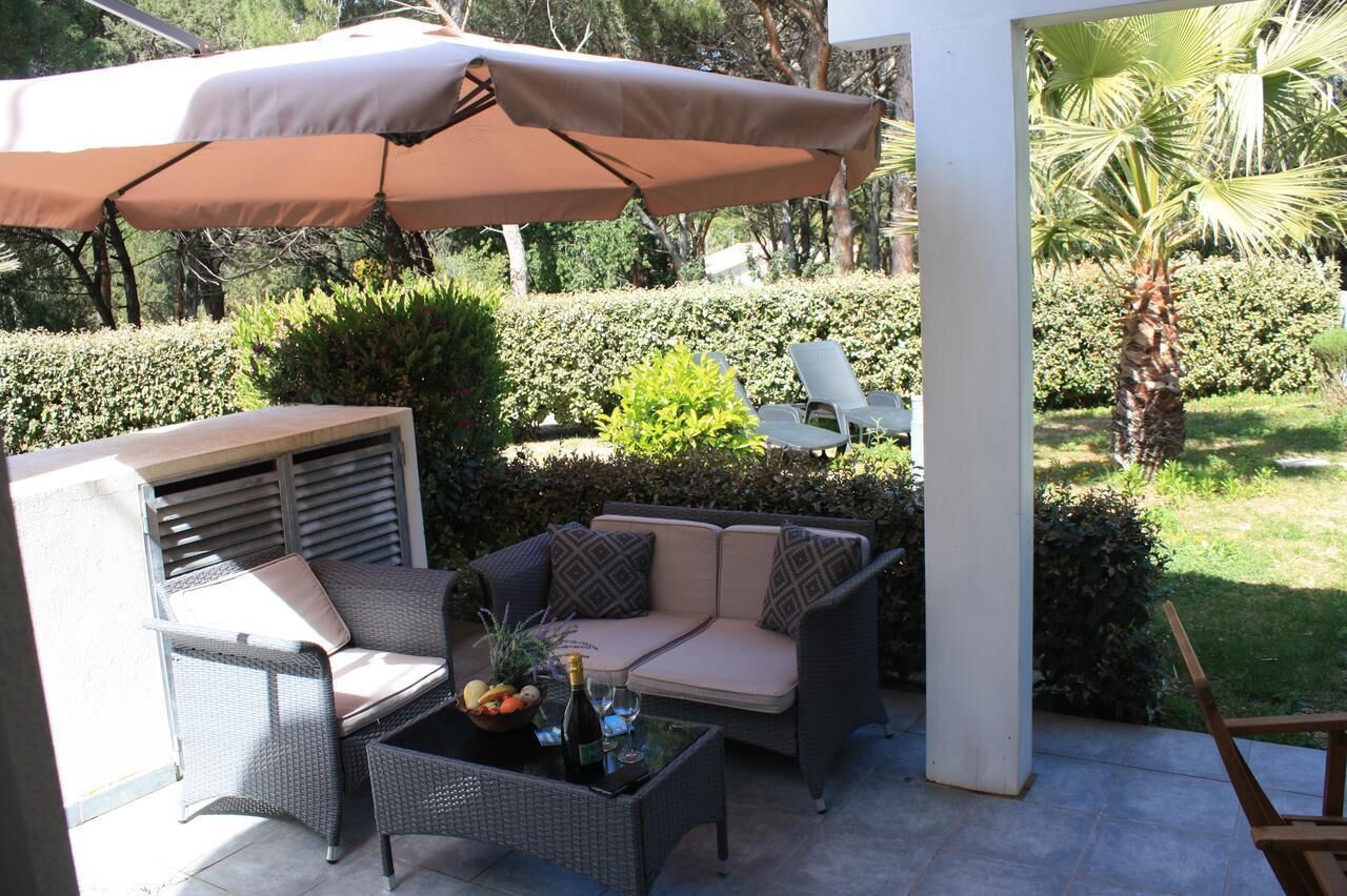 An outdoor patio with wicker furniture, a table with a bottle and glasses, and a large umbrella.