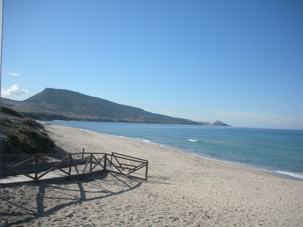 A beach with a wooden walkway leading to the water, a clear sky, and a hilly landscape in the background. - Villa Ginepro (Valledoria)