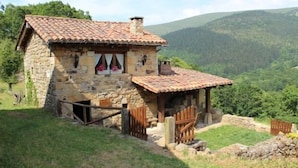 A stone house with a tiled roof, surrounded by a stone wall and wooden gates, set against a mountainous backdrop. - Cabin in the mountain (full rental) for 2/3 people. Pets allowed (Luena)