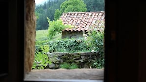A rustic stone wall with a tiled roof structure, surrounded by lush greenery and a forested backdrop. - Cabin in the mountain (full rental) for 2/3 people. Pets allowed (Luena)
