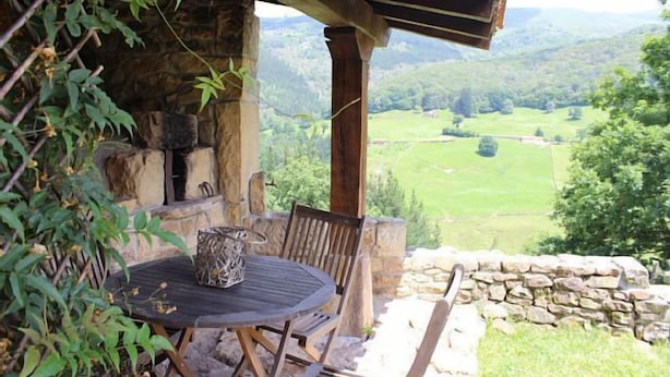 A rustic outdoor seating area with a stone wall and a view of a green valley. - Cabin in the mountain (full rental) for 2/3 people. Pets allowed (Luena)