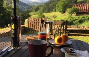 A table with a bottle of wine, a mug, a jar of jam, bread, and oranges.