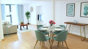 A modern living room with a glass dining table, green chairs, and a wooden coffee table. There is a sofa, a potted plant, and artwork on the walls. - Albareda 1 - One Bedroom Apartment, Sleeps 4 (Sevilla)