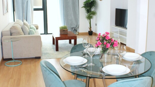 A modern living room with a glass dining table set for four, a sofa, a coffee table, and a TV on the wall. - Albareda 1 - One Bedroom Apartment, Sleeps 4 (Sevilla)