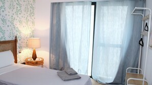 A hotel room with a bed, a bedside lamp, a wicker side table, and a window with curtains. - Albareda 1 - One Bedroom Apartment, Sleeps 4 (Sevilla)