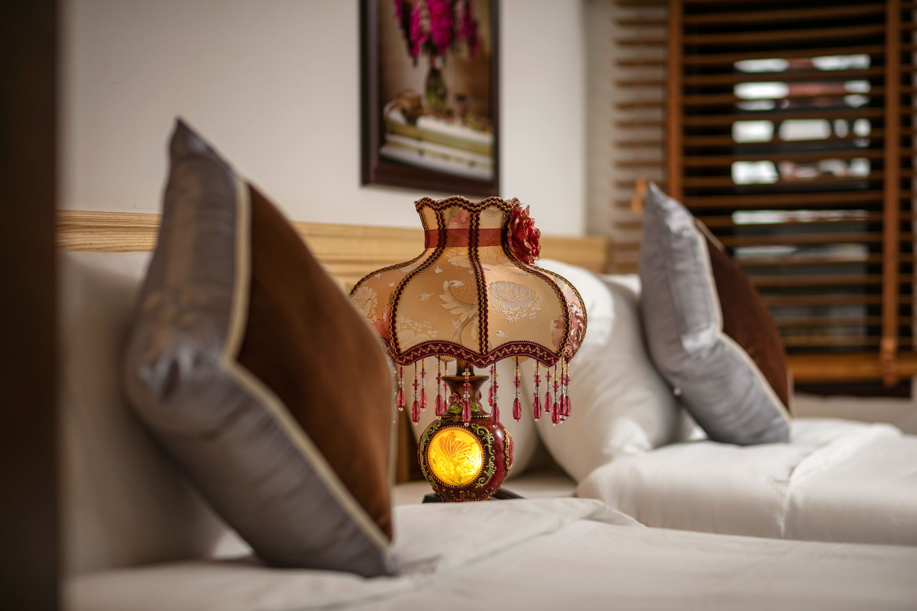 Una cama con ropa blanca, una lámpara decorativa y almohadas.