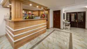 A reception area with a wooden counter, a tiled floor with a decorative border, and a view into the kitchen area.