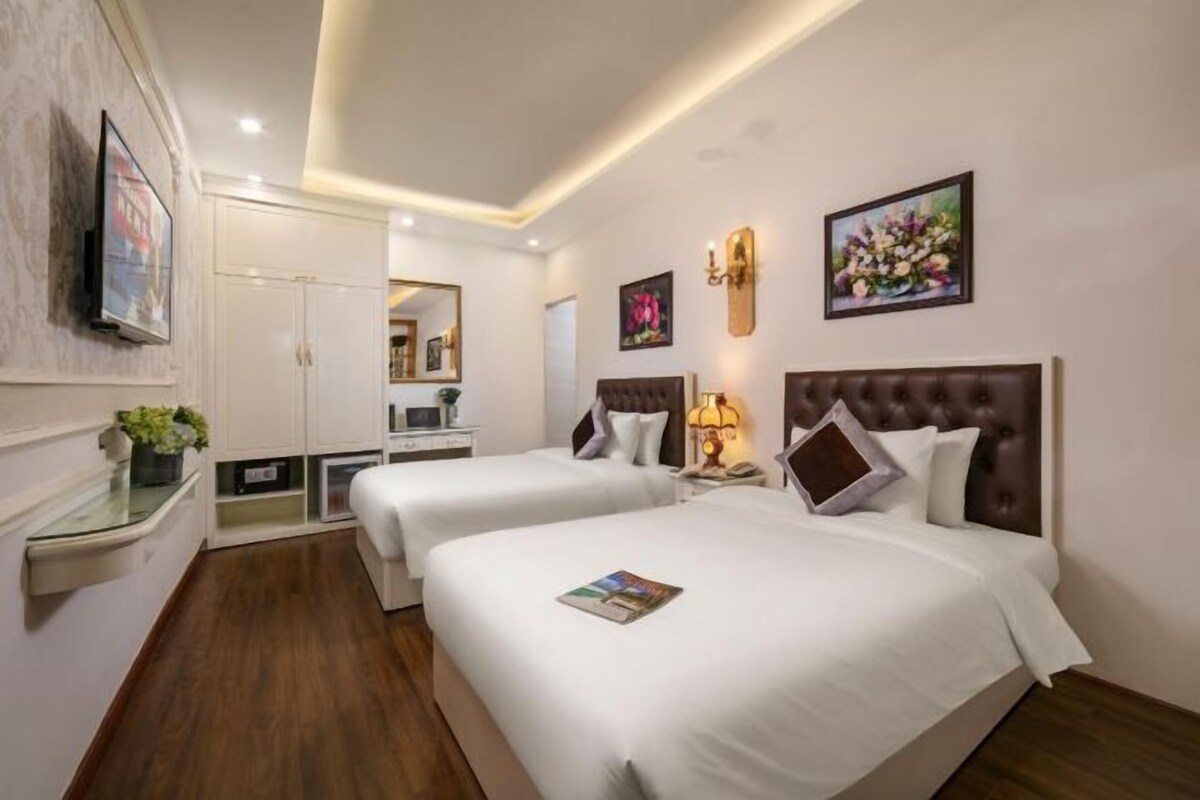 A hotel room with two beds, a desk, a mirror, and a small kitchenette.
