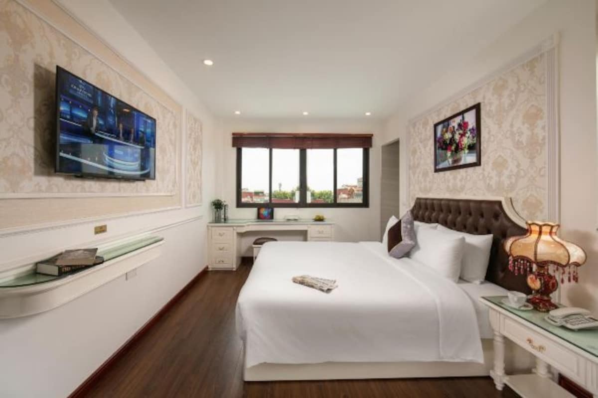 Ein Hotelzimmer mit einem großen Bett, einem an der Wand befestigten Fernseher, einem Schreibtisch mit Stuhl, einem Fenster mit Blick und einem Nachttisch mit Lampe.