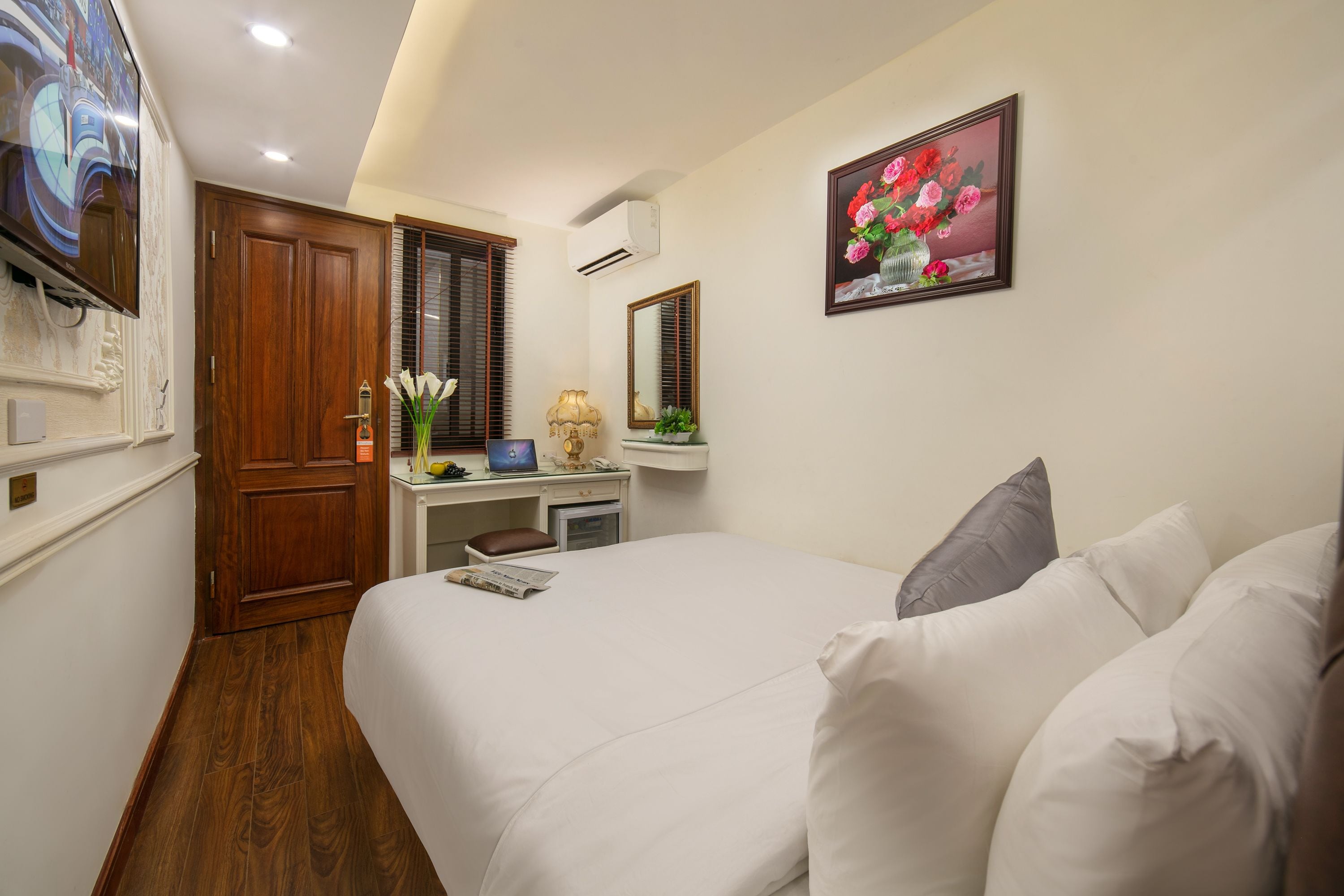 Habitación de hotel con cama, escritorio con computadora, espejo y televisor en la pared.