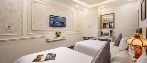 A hotel room with two beds, a television on the wall, a mirror, and a decorative lamp.