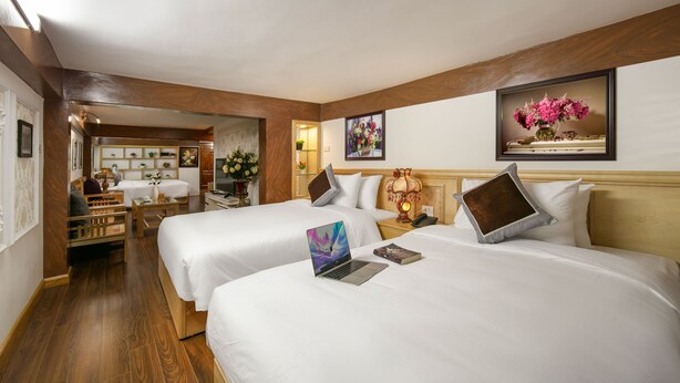 A hotel room with two beds, a desk, and a chair. There are framed pictures on the walls and a wooden ceiling.