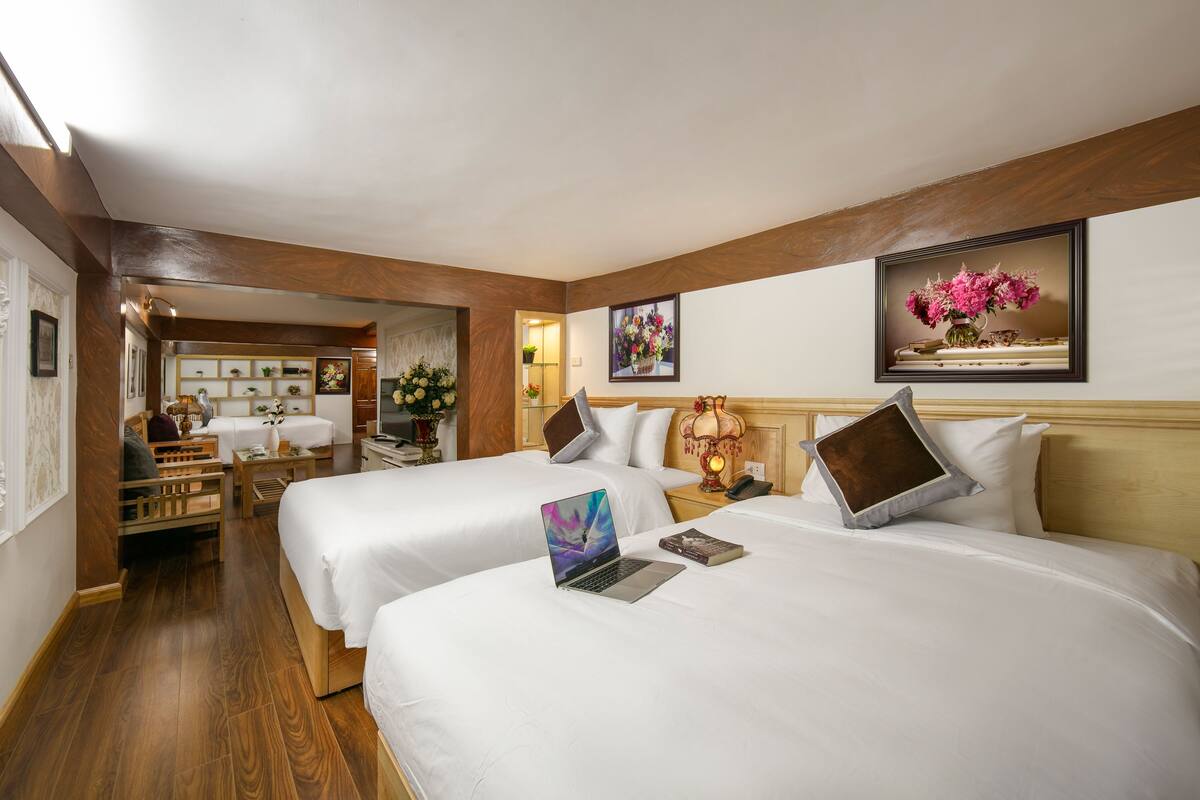 Camera d'albergo con due letti, una scrivania e una sedia. Alle pareti ci sono quadri incorniciati e il soffitto è in legno.