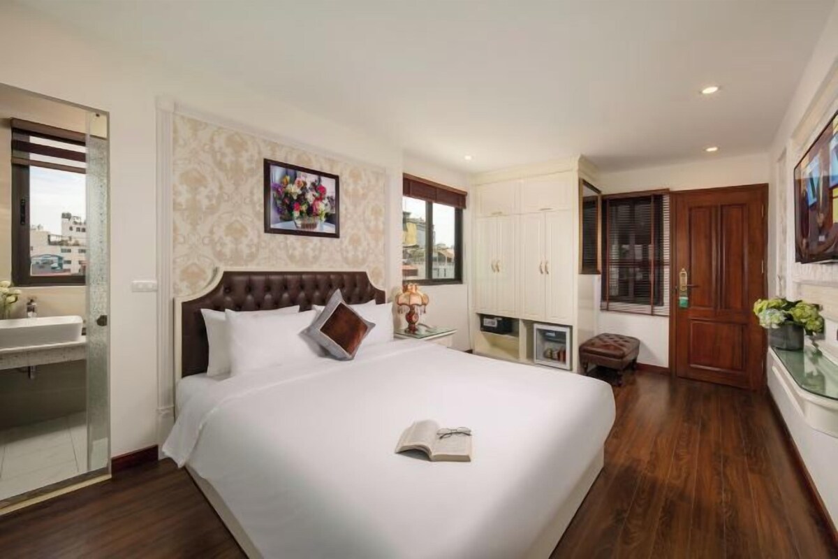 A hotel room with a large bed, a bedside table, a mirror, a window, and a door.