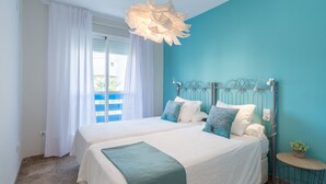 A bedroom with two beds, a teal accent wall, a hanging light fixture, and a small round table with a plant. - MalagaSuite Lux Beach & Pool (Torremolinos)