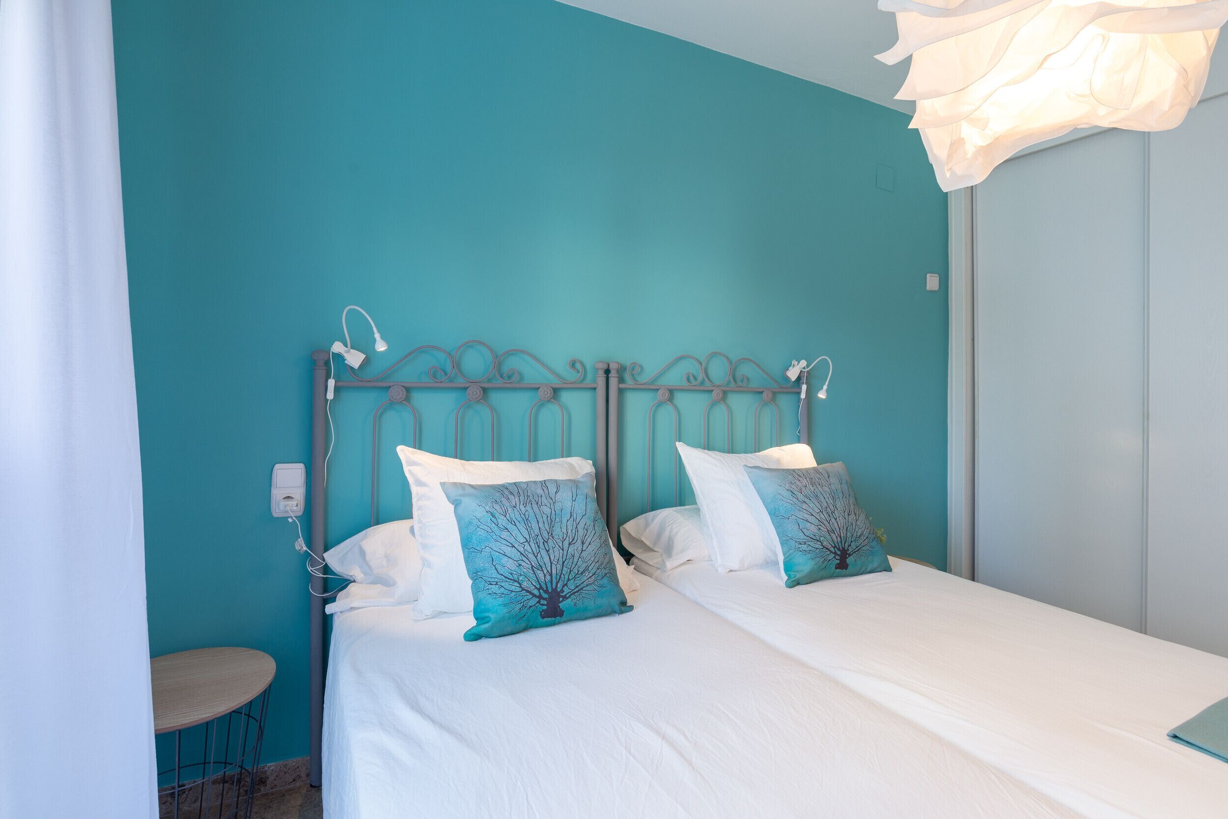 A bedroom with a teal wall, a metal bed frame, white bedding, and a small round table.