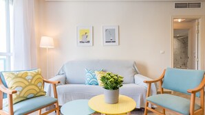 A cozy living room with a sofa, two armchairs, a small round table with a plant, and two framed artworks on the wall. - MalagaSuite Lux Beach & Pool (Torremolinos)