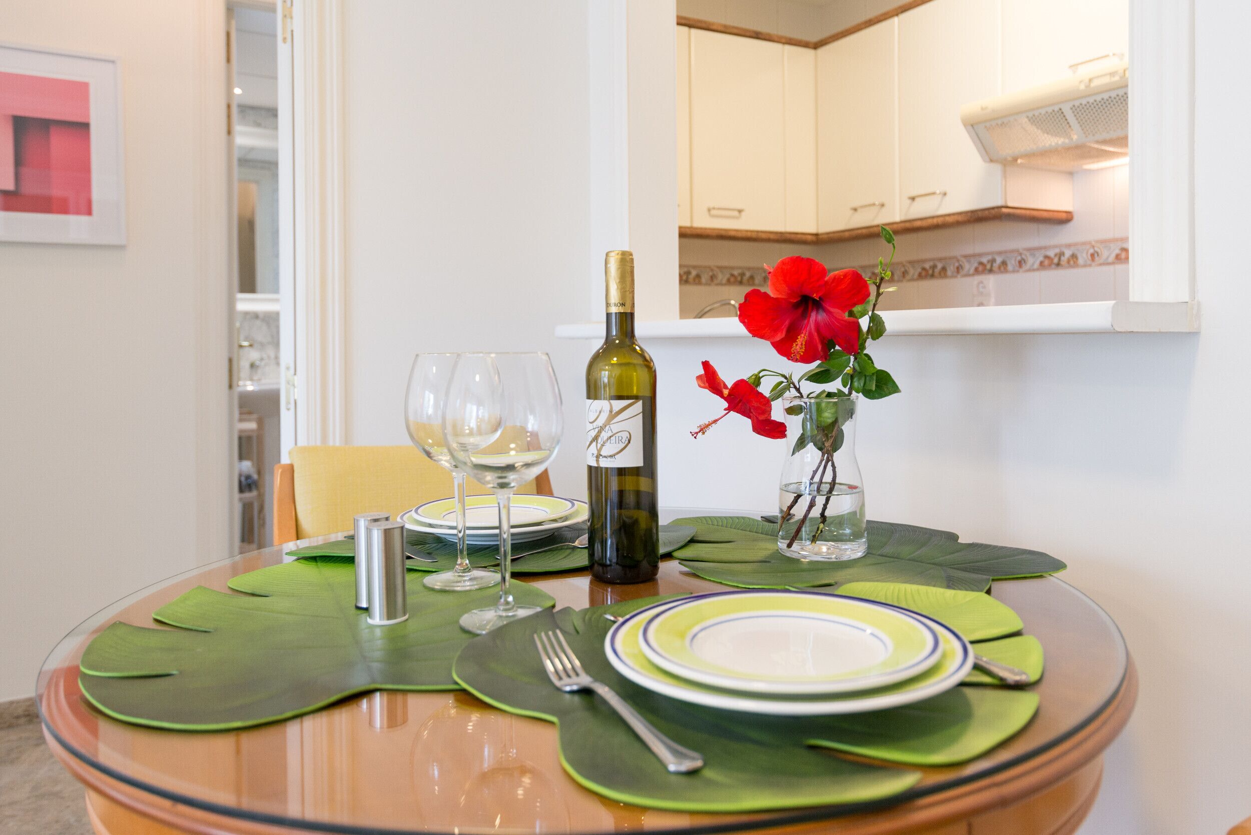 Una mesa de comedor con platos, una botella de vino, copas y un jarrón con flores.