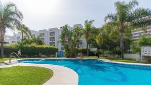 A swimming pool with a curved edge, surrounded by well-maintained grass and palm trees. - MalagaSuite Lux Beach & Pool (Torremolinos)