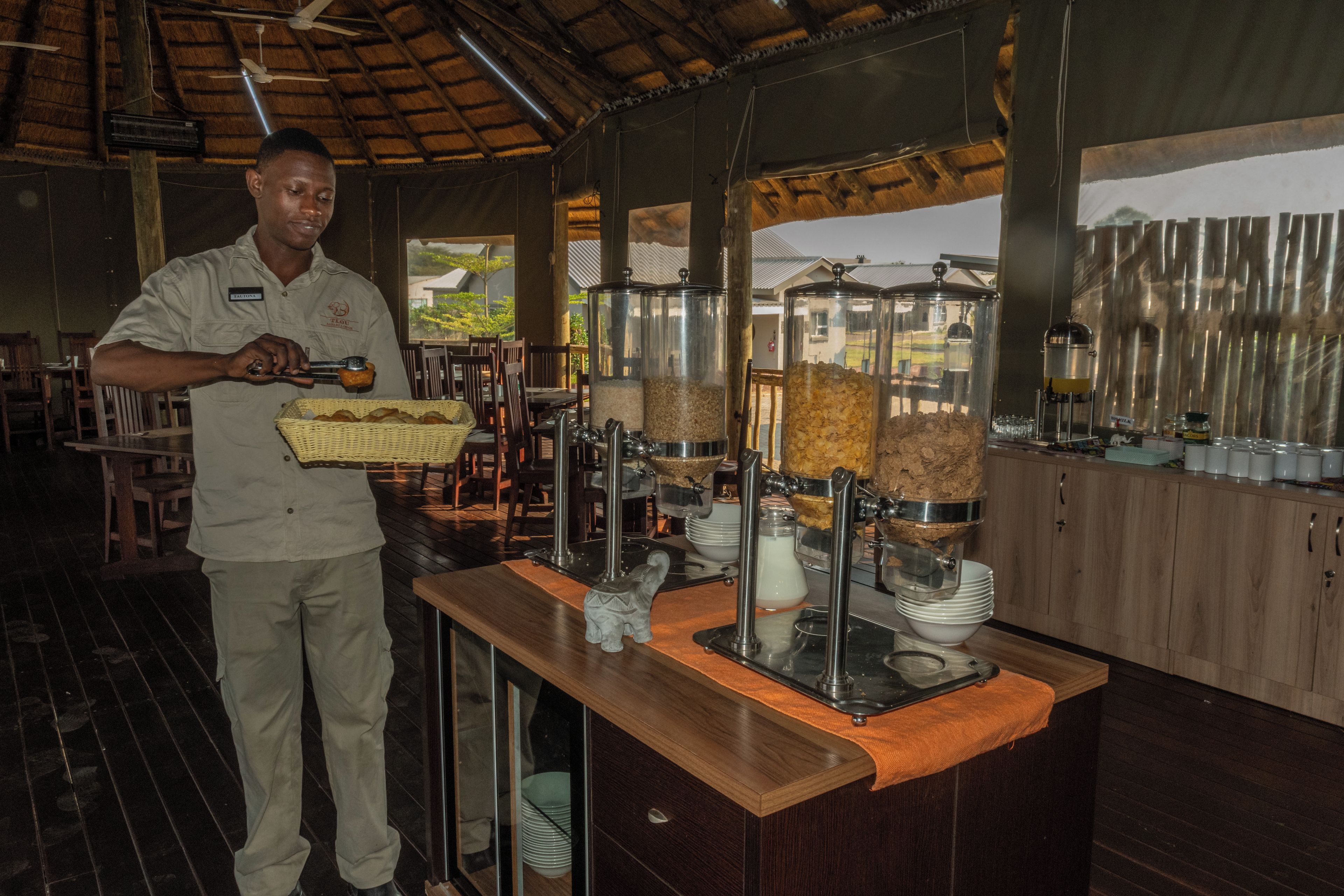 A buffet setup with a person serving food, a variety of food containers, and a wooden counter.