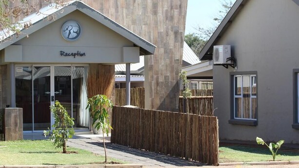 A reception area with a sign, a small tree, and a fence. - Tlou Safari Lodge (Kasane)