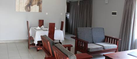 A dining area with a table set for four, wooden chairs, and a large elephant artwork on the wall.