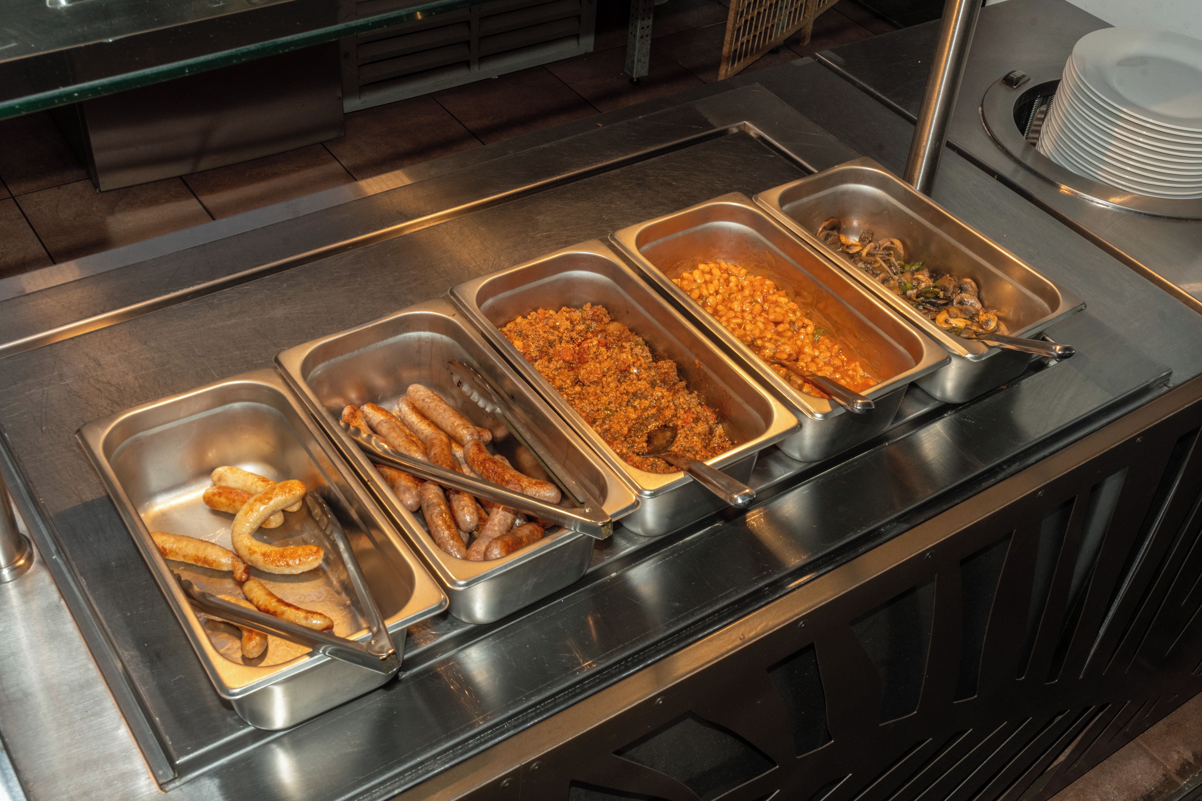 A buffet with various food options including sausages, baked beans, and a casserole dish.
