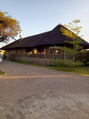 A building with a thatched roof, a paved entrance, and a wooden fence. - Tlou Safari Lodge (Kasane)