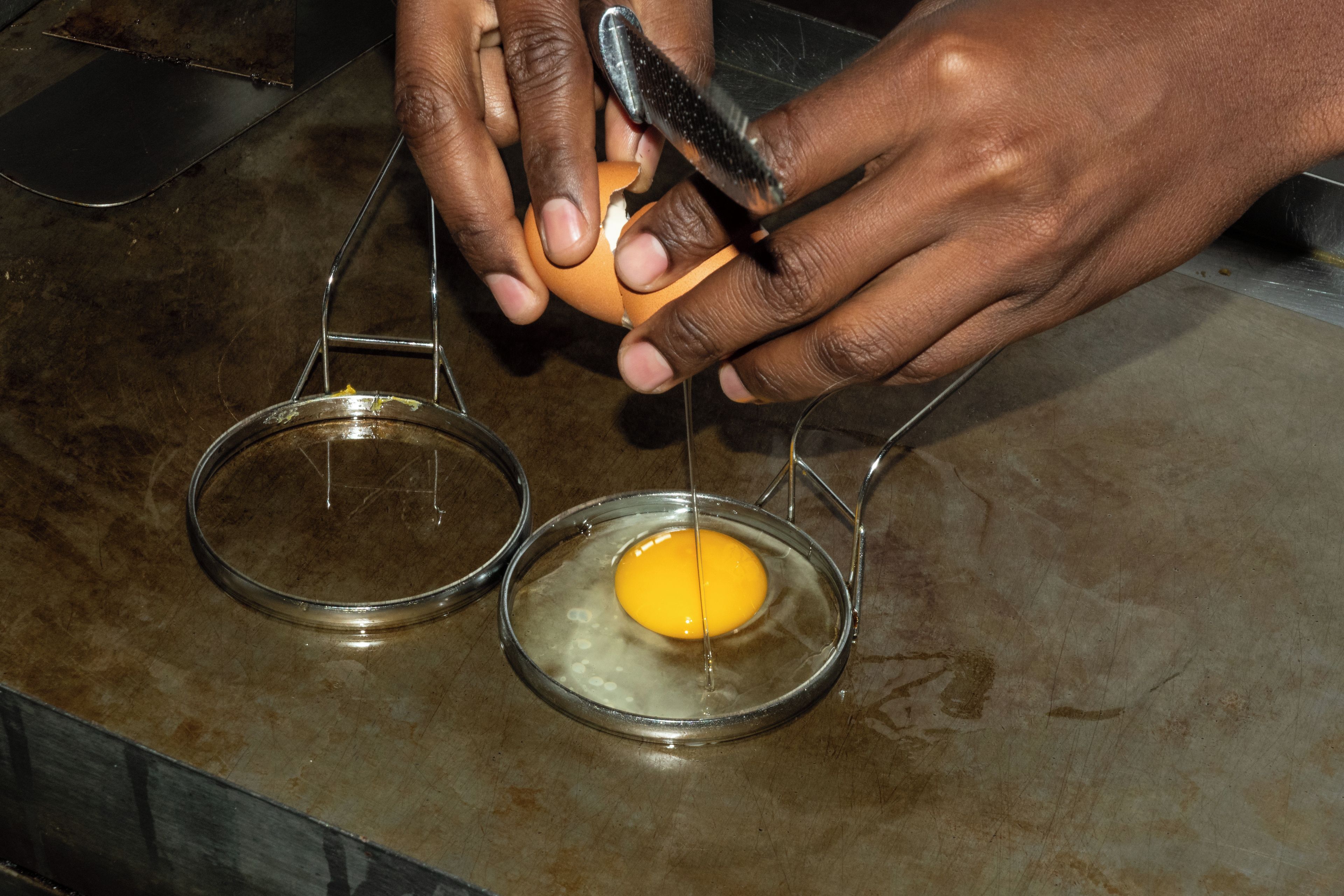 A person cracking an egg into a small glass bowl.