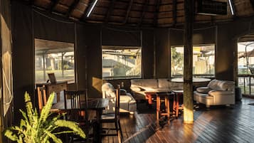 A room with a wooden floor, a sofa, a table, and a chair. There are windows and a ceiling fan.