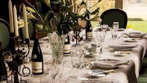 Una mesa de comedor lista para una comida, con botellas de vino, copas y un florero con plantas.