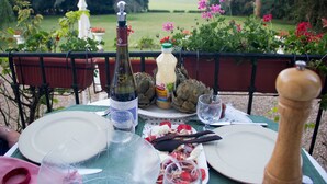 Una mesa al aire libre con una botella de vino, una botella de mostaza, alcachofas y platos con comida.