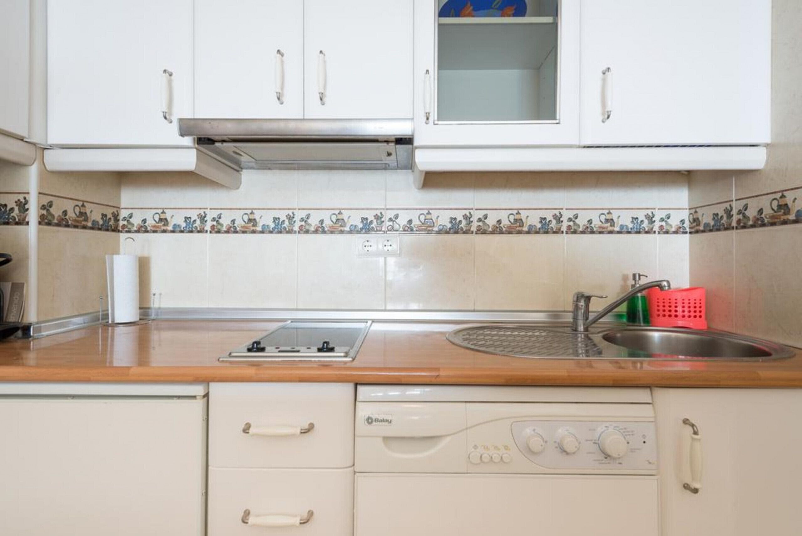 A kitchen with white cabinets, a wooden countertop, a built-in stove, a sink, and a dishwasher.