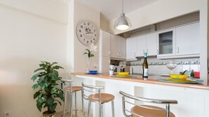 A kitchen with white cabinets, a bar area with stools, a potted plant, and a clock on the wall.