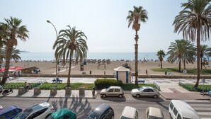 A coastal street with parked cars, palm trees, and a beach in the background.