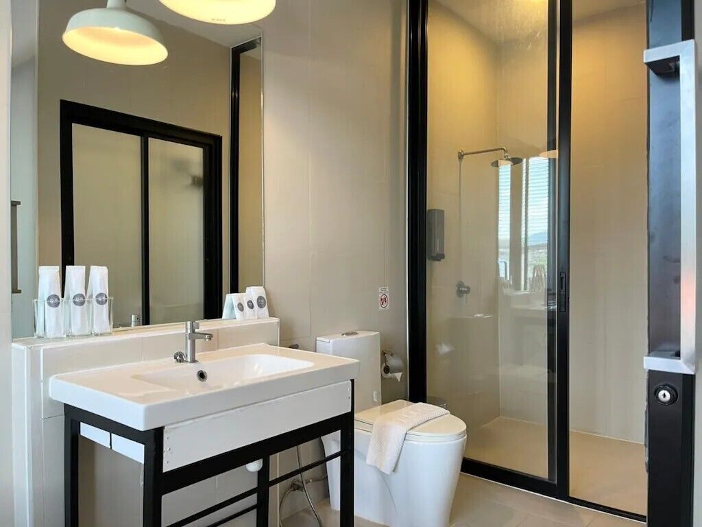 A modern bathroom with a white sink, mirror, and toilet. It includes a glass-enclosed shower area.