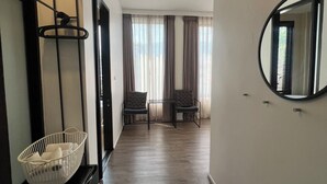 A hallway with a wooden floor, a white wall, and a round mirror. There are two chairs and a small table in the distance. - POR Santitham (Chiang Mai)