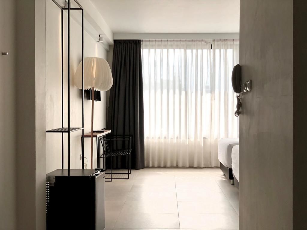 A hotel room with a bed, a desk, a lamp, and a large window with sheer curtains.