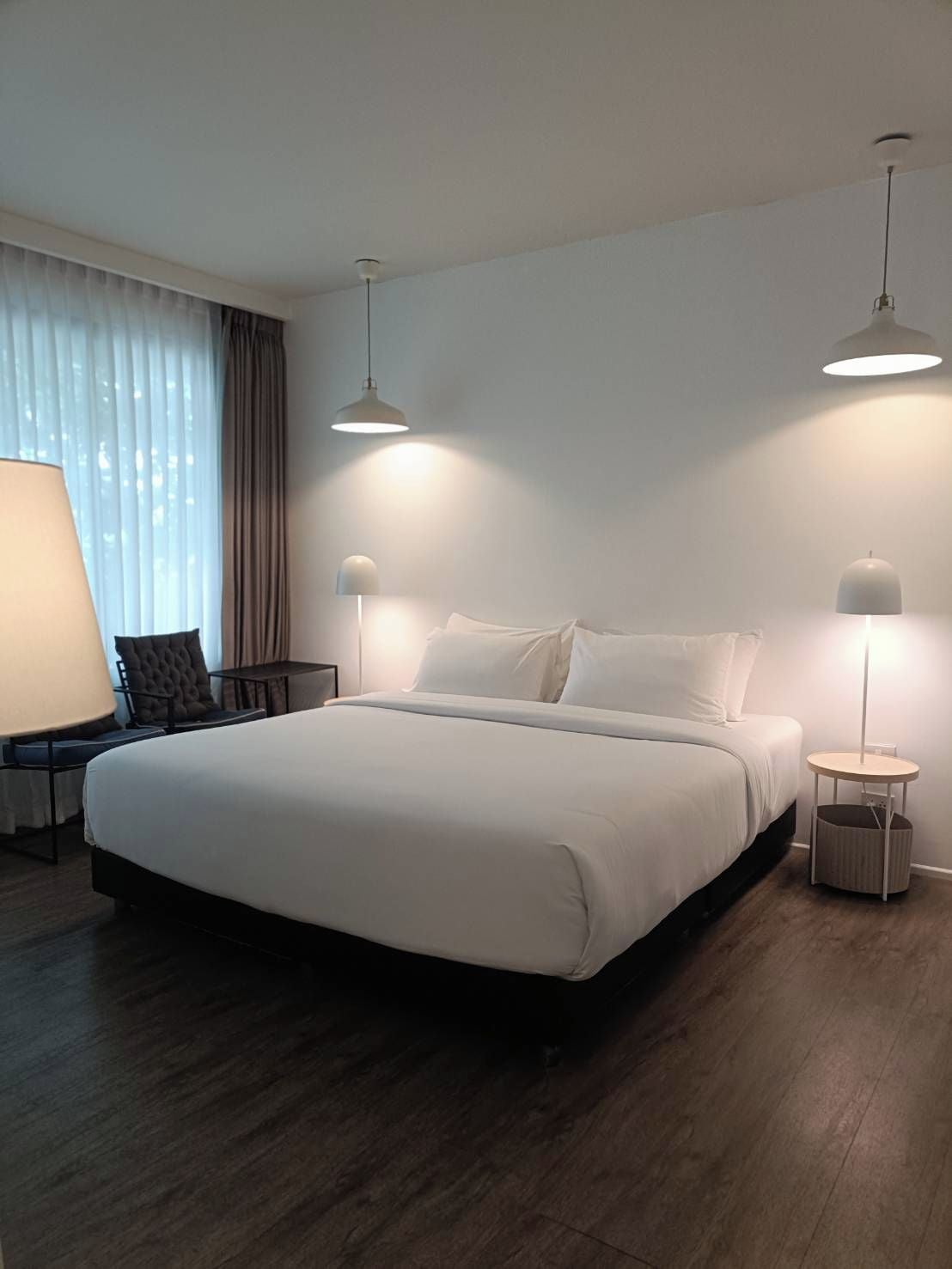 Et hotelværelse med en stor seng, to sengeborde med lamper, en stol og et bord.