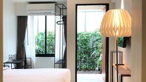 A hotel room with a bed, a desk, an air conditioning unit, a lamp, and a view of greenery outside. - POR Santitham (Chiang Mai)