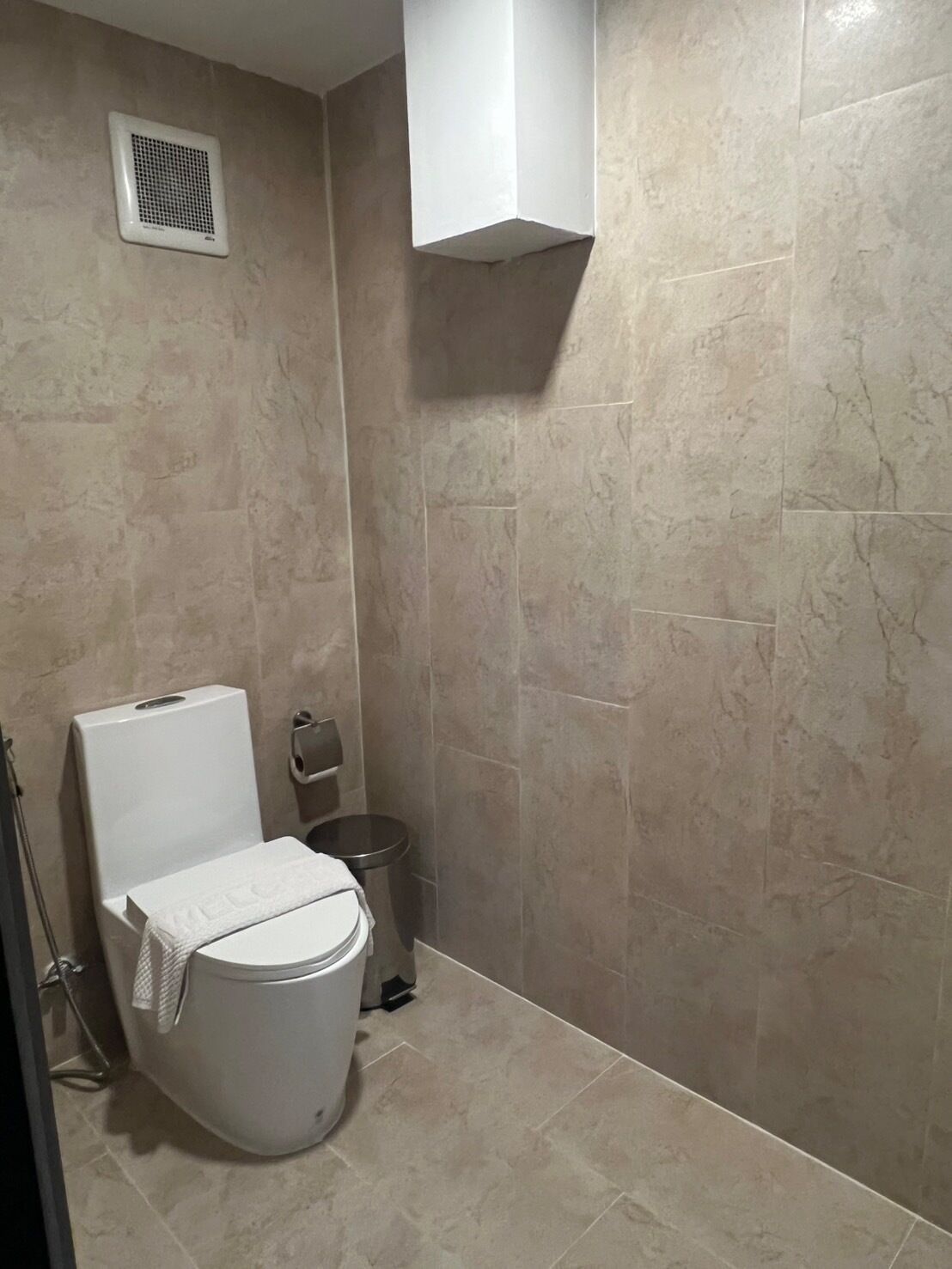 Un baño con inodoro, un cubo de basura y un perchero para toallas.