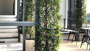 A modern outdoor seating area with a metal railing, potted plants, and a table with chairs. - POR Santitham (Chiang Mai)