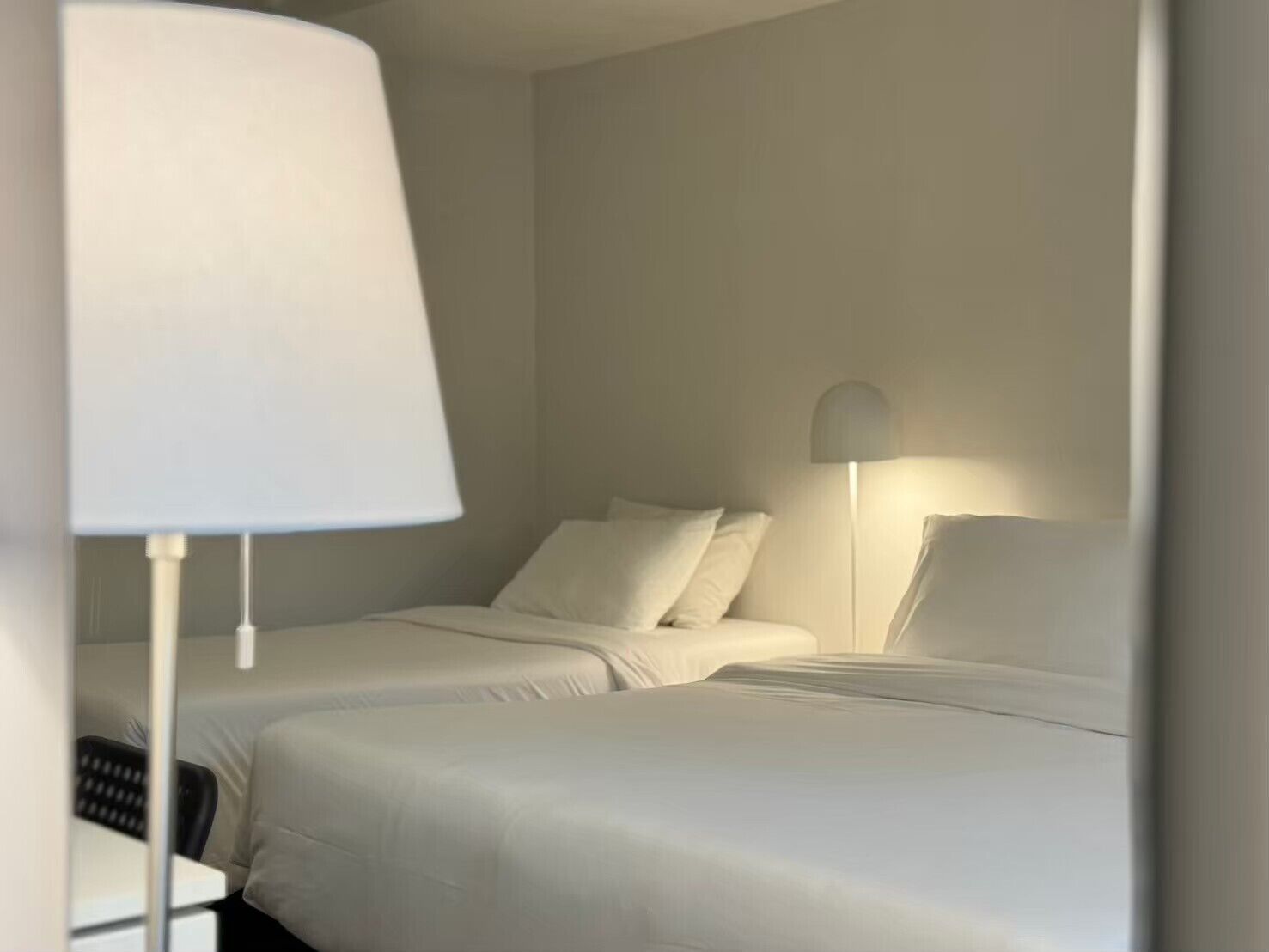 A hotel room with two beds, a desk, and a lamp.