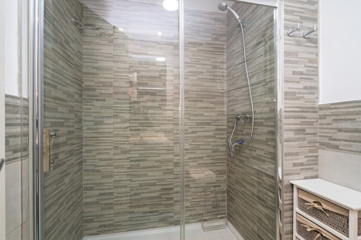A glass-enclosed shower with a tiled wall and a white vanity with a basket.