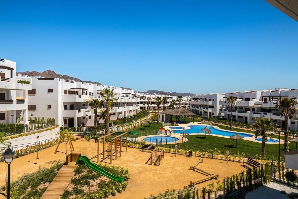A resort with multiple white buildings, a central pool area with a slide, and a clear view of the surrounding landscape.
