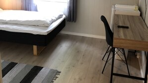 A bedroom with a bed, a desk, and a chair. There is a window with curtains, a radiator, and a TV on the wall. - Mosjøen Hybelhus (Vefsn)