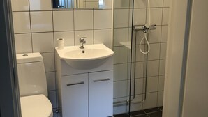 A modern bathroom with a toilet, sink, and glass shower enclosure. - Mosjøen Hybelhus (Vefsn)