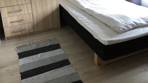 A bedroom with a bed, a wooden wardrobe, a mirror, a bedside lamp, and a striped rug. - Mosjøen Hybelhus (Vefsn)