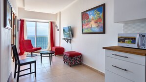 Una sala de estar moderna con un sillón rojo, una mesita, un reposapiés rojo, un televisor y un microondas.
