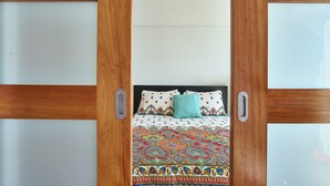 Una habitación con cama, puerta de madera y una colcha estampada.